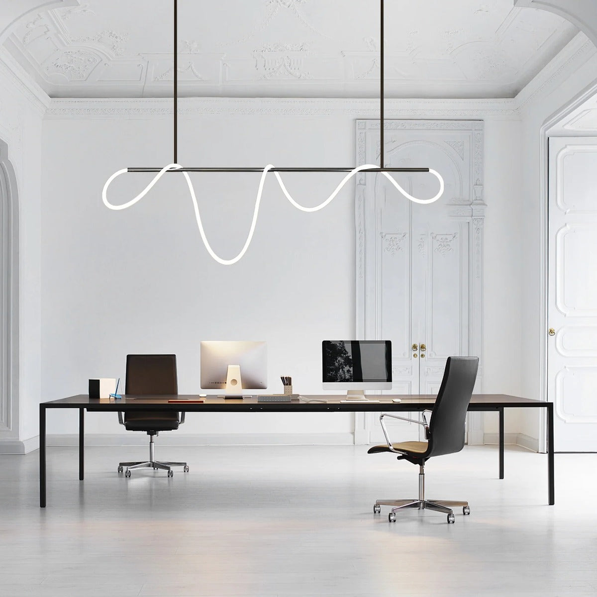 Black Ondine wave LED linear pendant light above a modern office desk