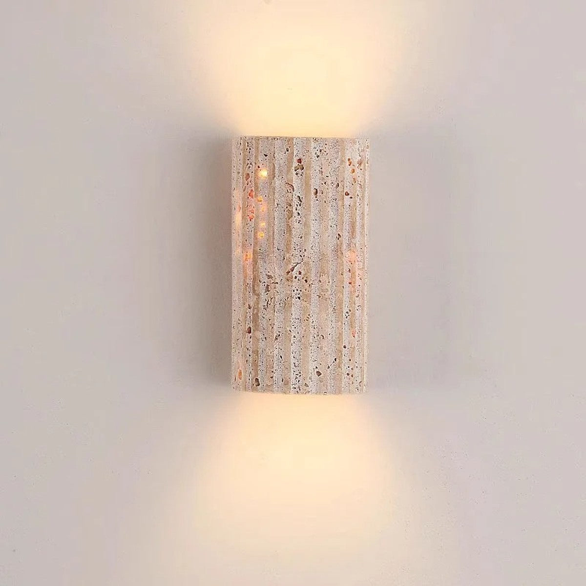 Talia fluted travertine wall sconce in natural stone, lit up and down