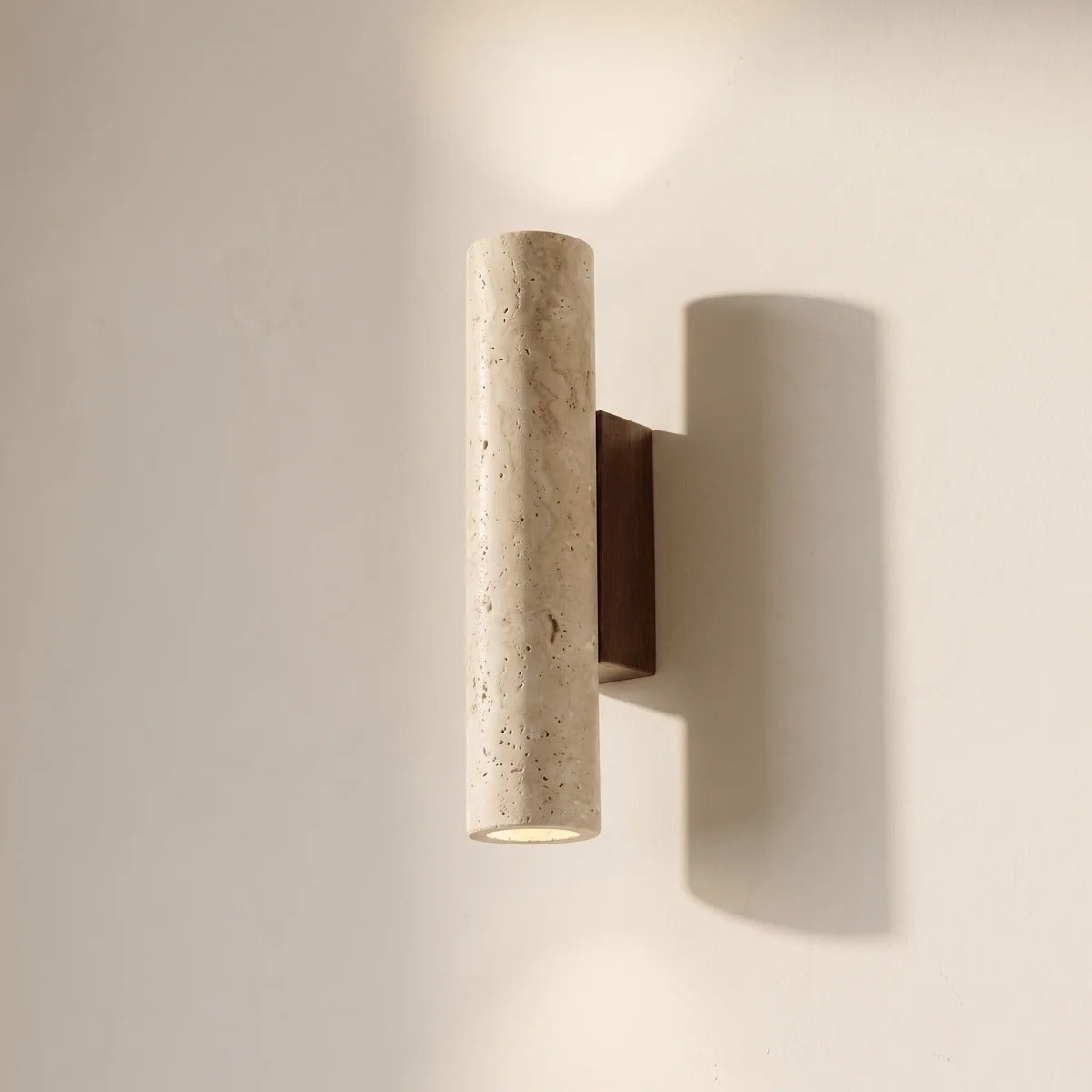 Tarra travertine cylinder wall sconce on a wood plate, glowing up and down
