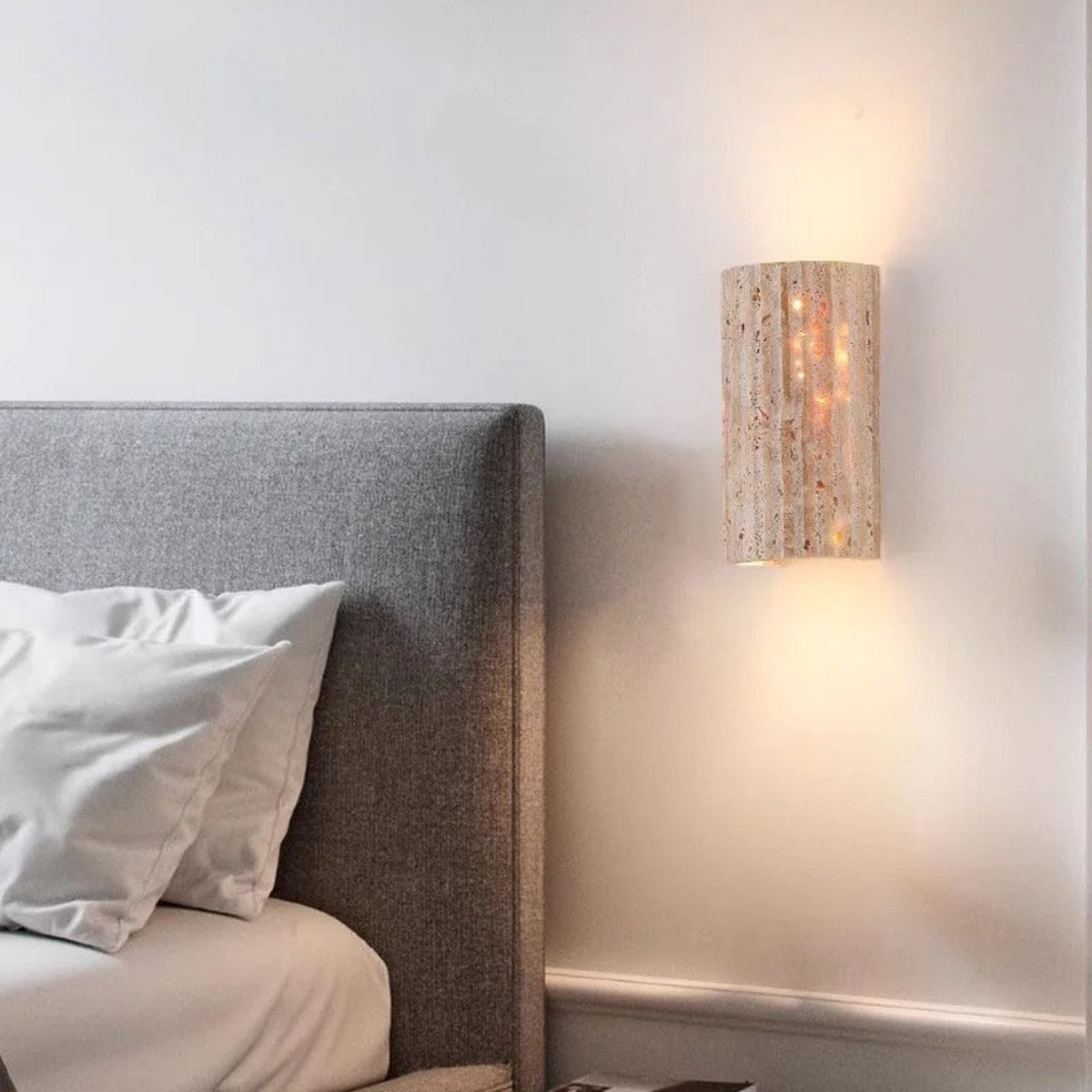 Talia travertine wall sconce glowing beside a bed