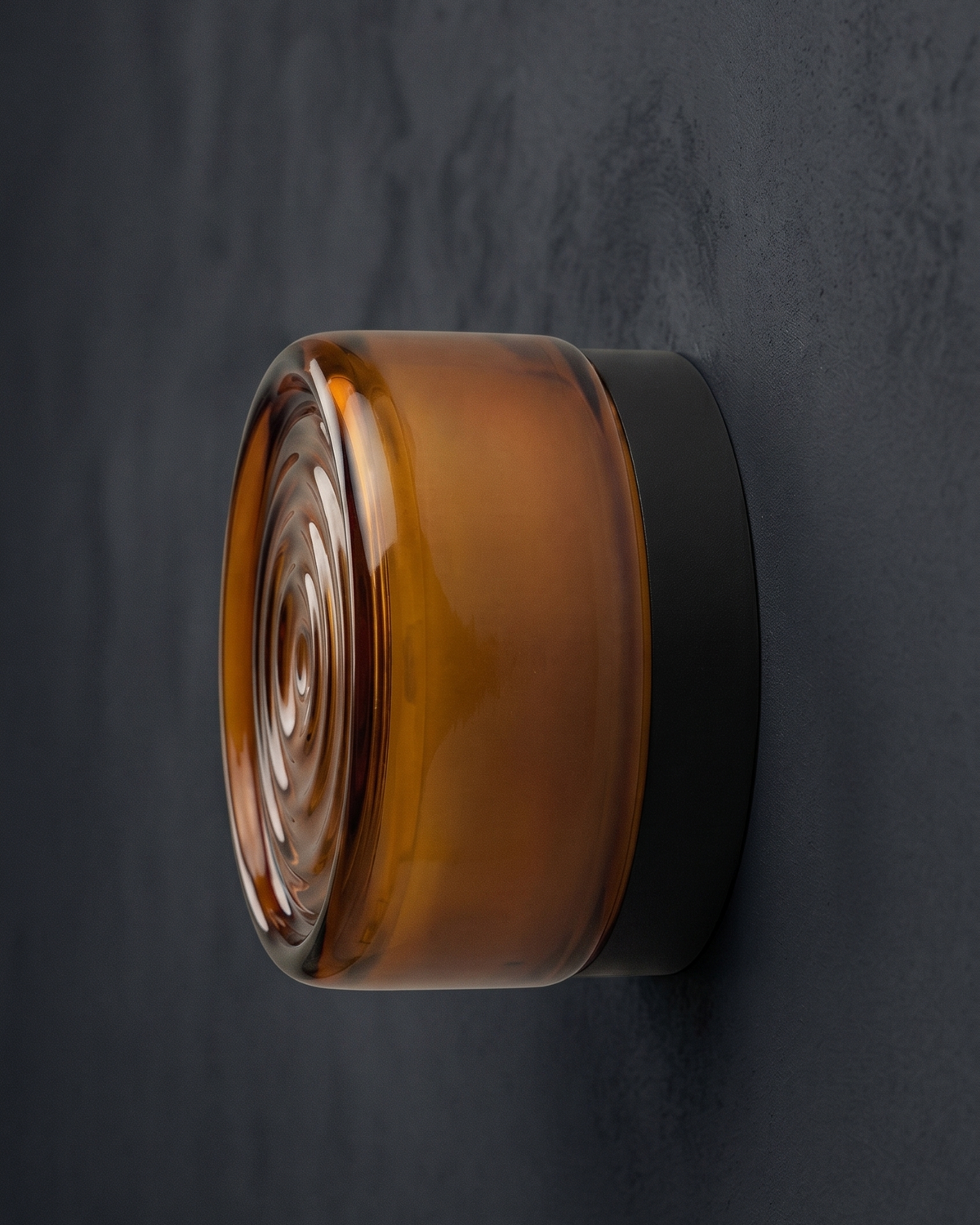 Orla round wall light with amber ripple shade on a dark wall