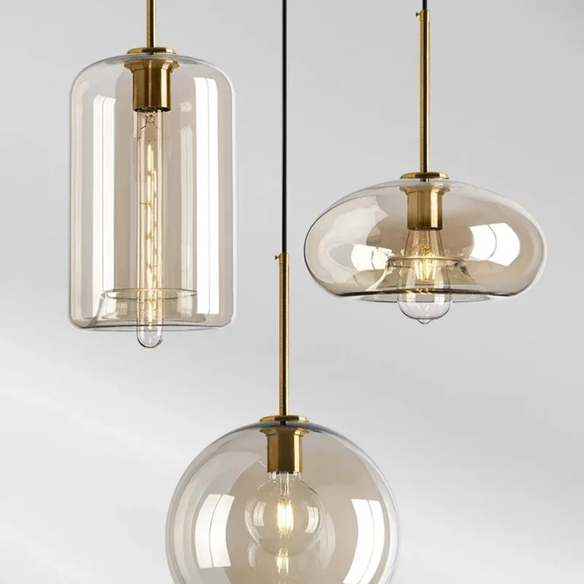Close-up of Ambra amber glass cylinder, oval and globe pendant lights with brass fittings and filament bulbs