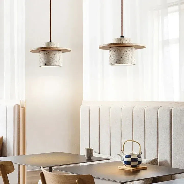 Two Avra travertine and natural wood pendant lights over a table in a bright dining interior