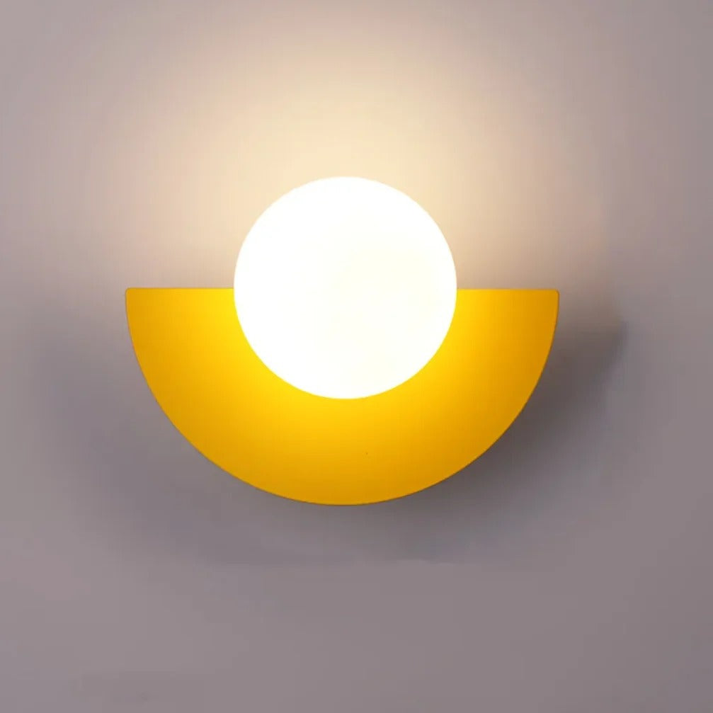 Cleo semicircle globe wall sconce in yellow, white glass globe with warm glow on a wall