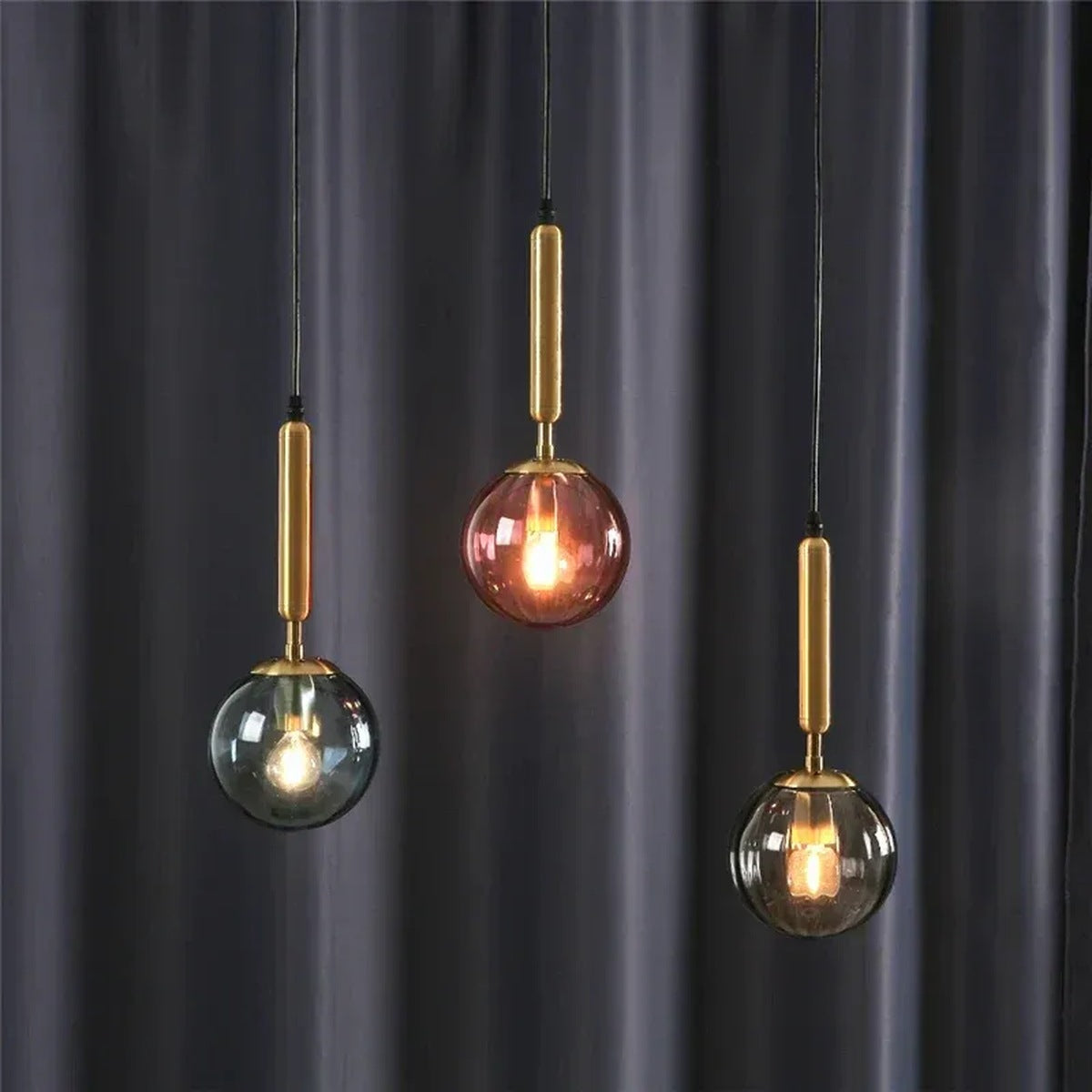 Three Coco ribbed glass globe pendant lights with gold stems in blue, pink and smoke gray glass