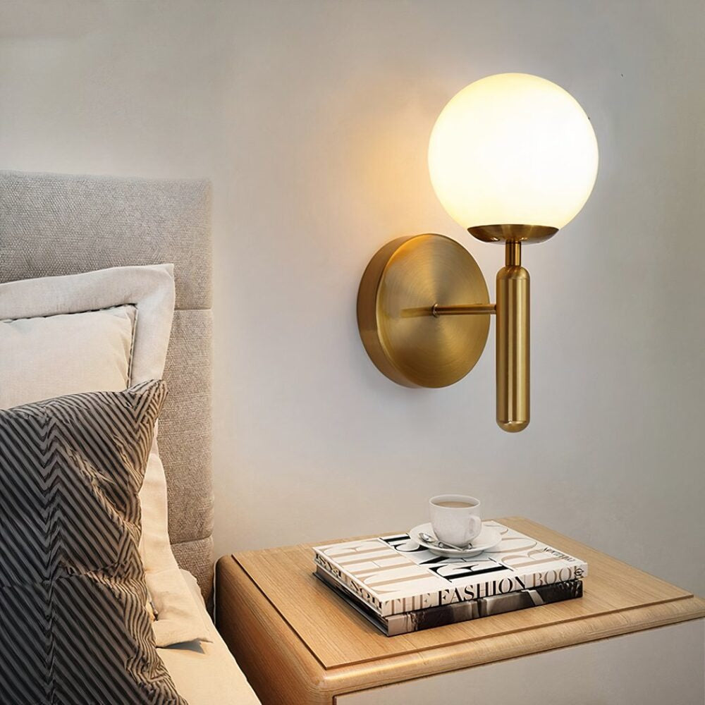 Elio globe wall sconce in gold beside a bed