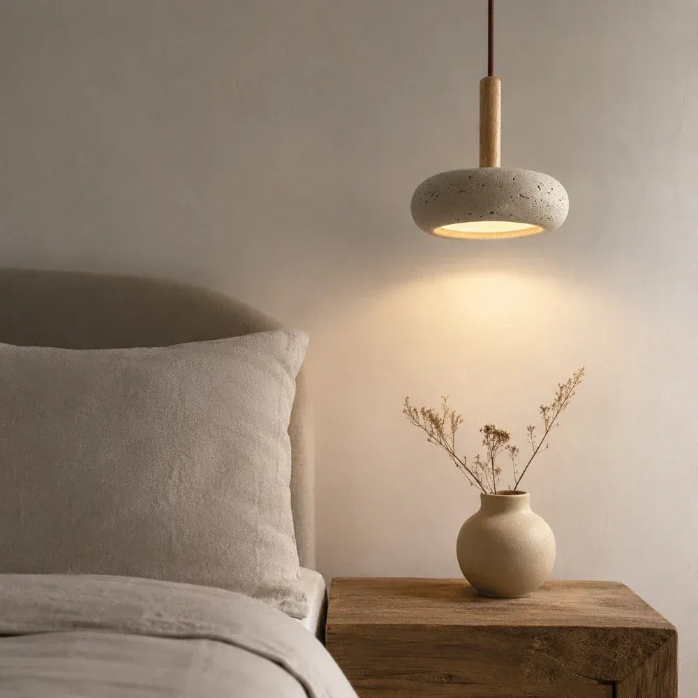Mila travertine pebble pendant light glowing above a wood nightstand beside a bed
