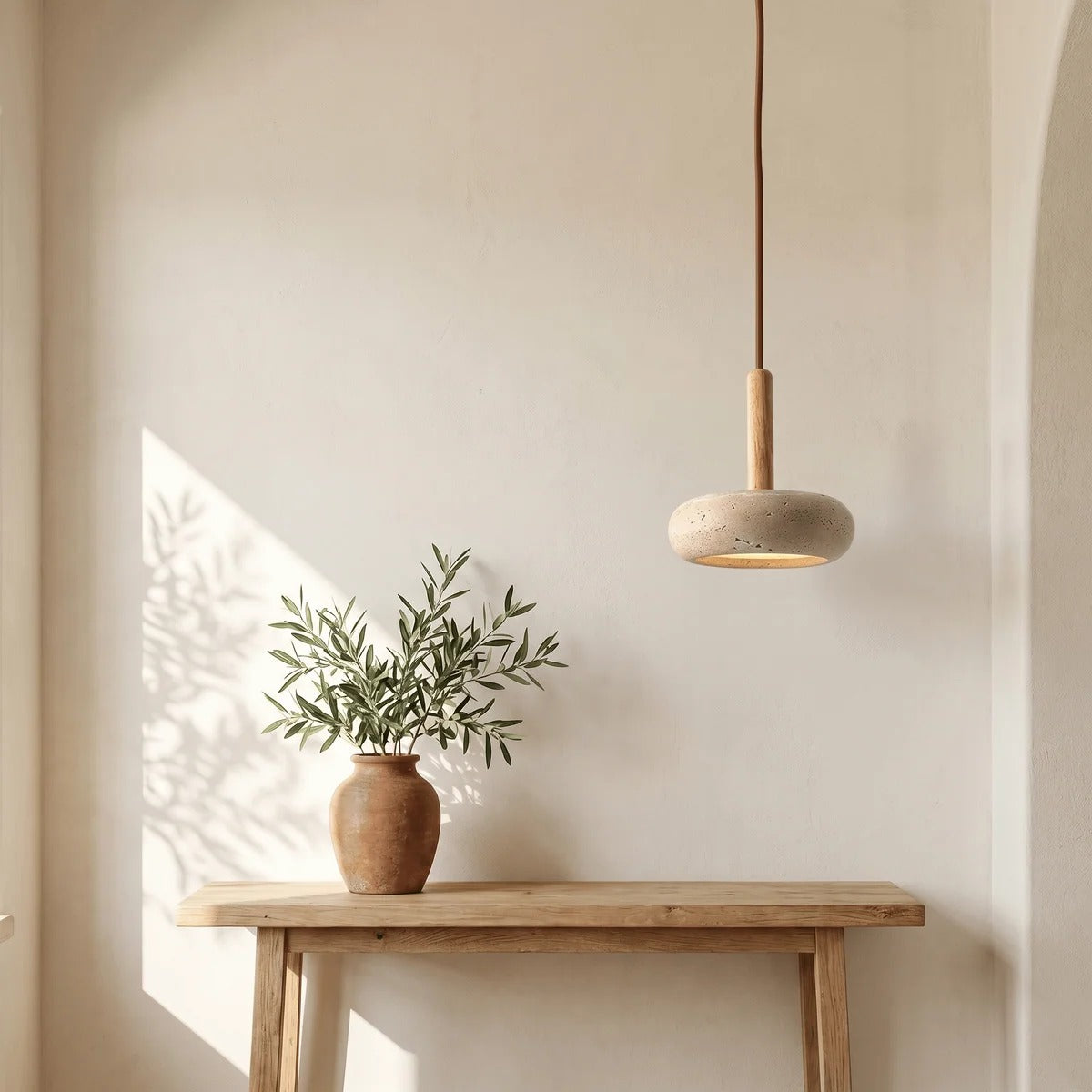 Mila travertine pebble pendant light above a wood console table with an olive branch vase