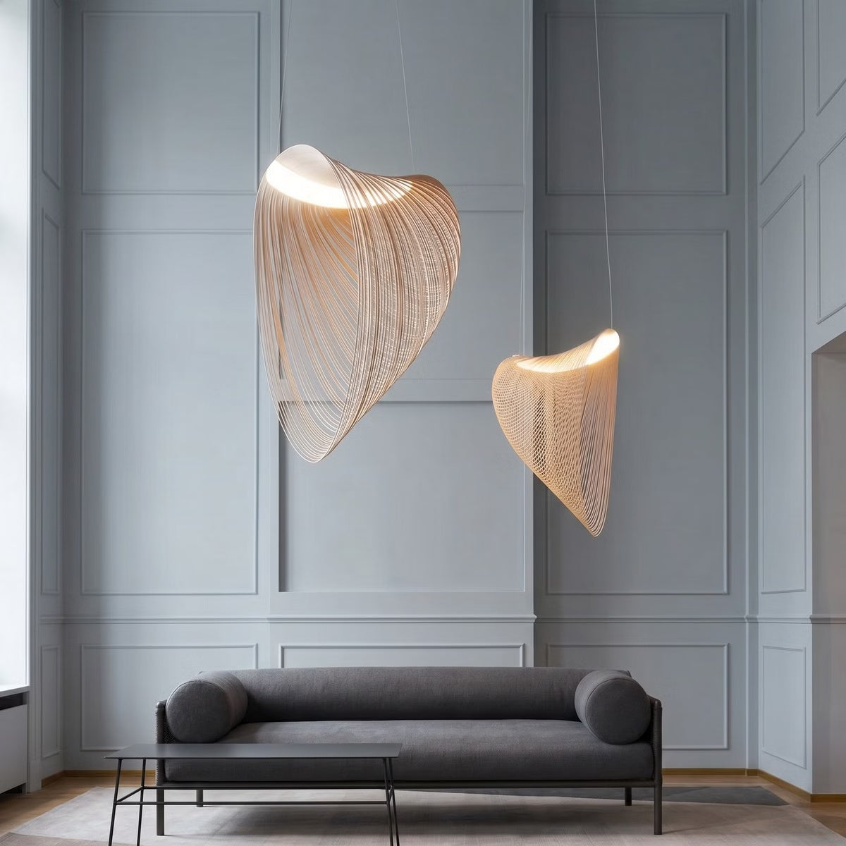 Two Wren LED pendants in large and small sizes above a grey sofa in a high-ceiling living room