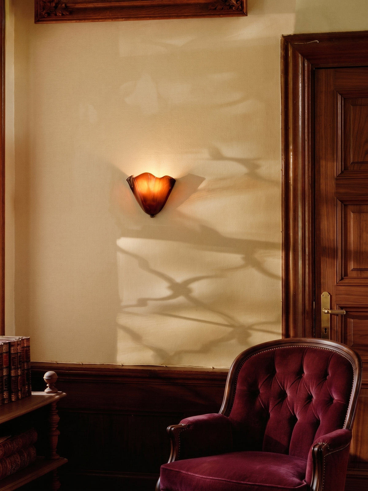 Amber brown Calla ruffled glass wall light glowing in a wood-paneled room