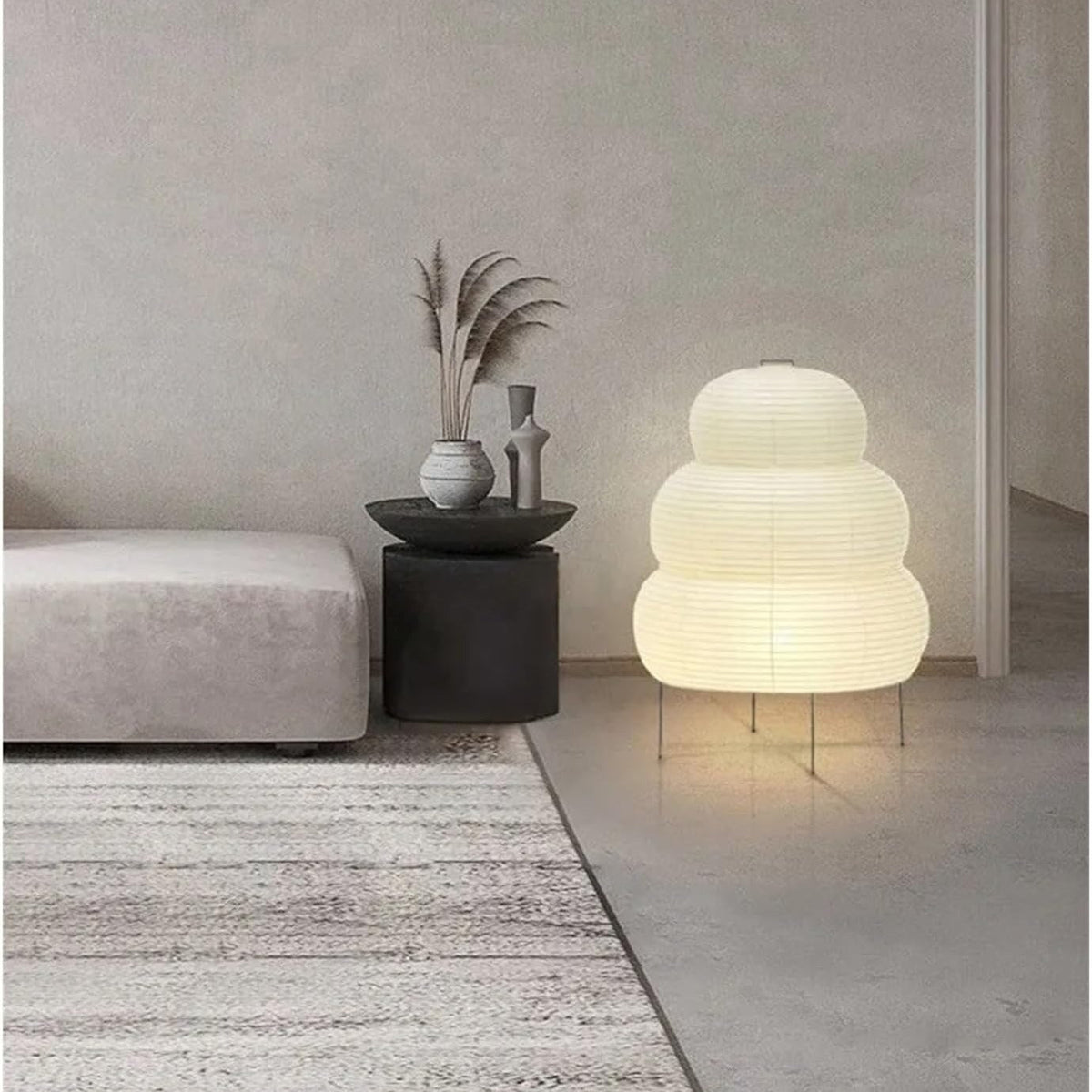 Kumo three-tier rice paper lantern lamp glowing on the floor beside a low sofa