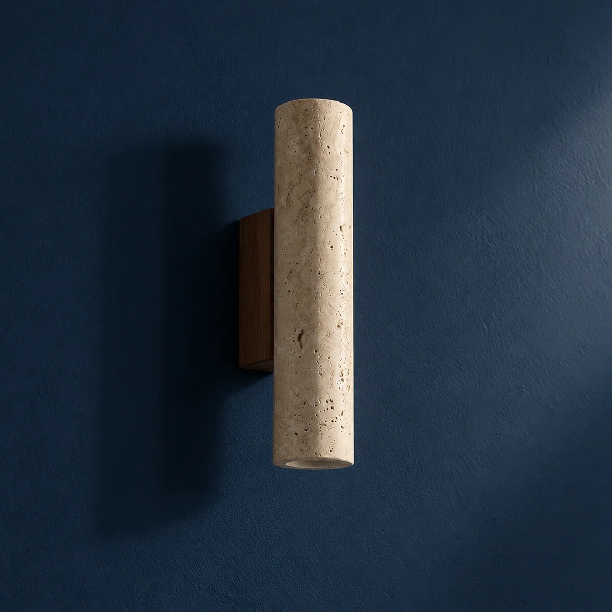 Tarra travertine wall sconce on a dark blue wall