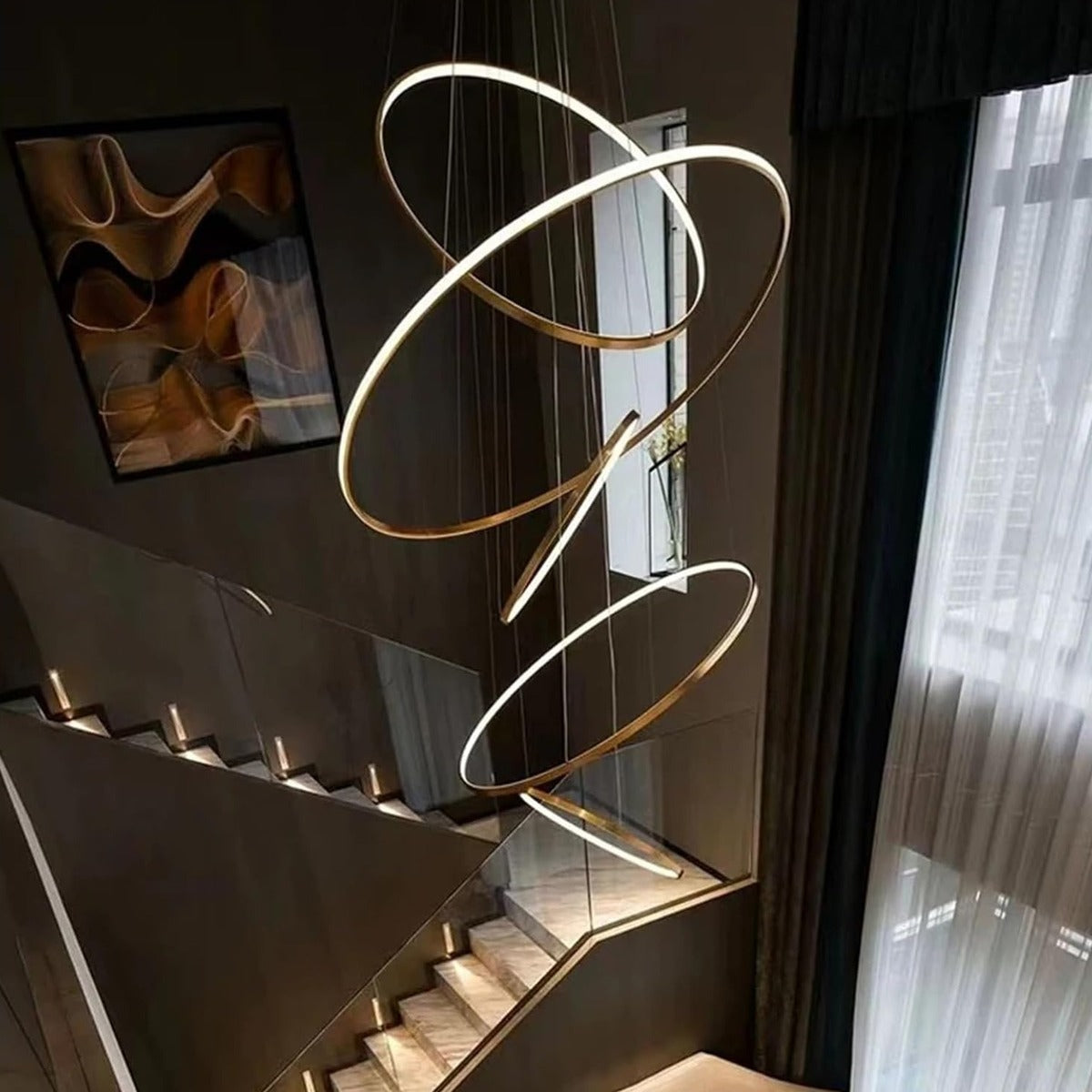 Gold Vela 5-ring LED chandelier hanging in a stairwell
