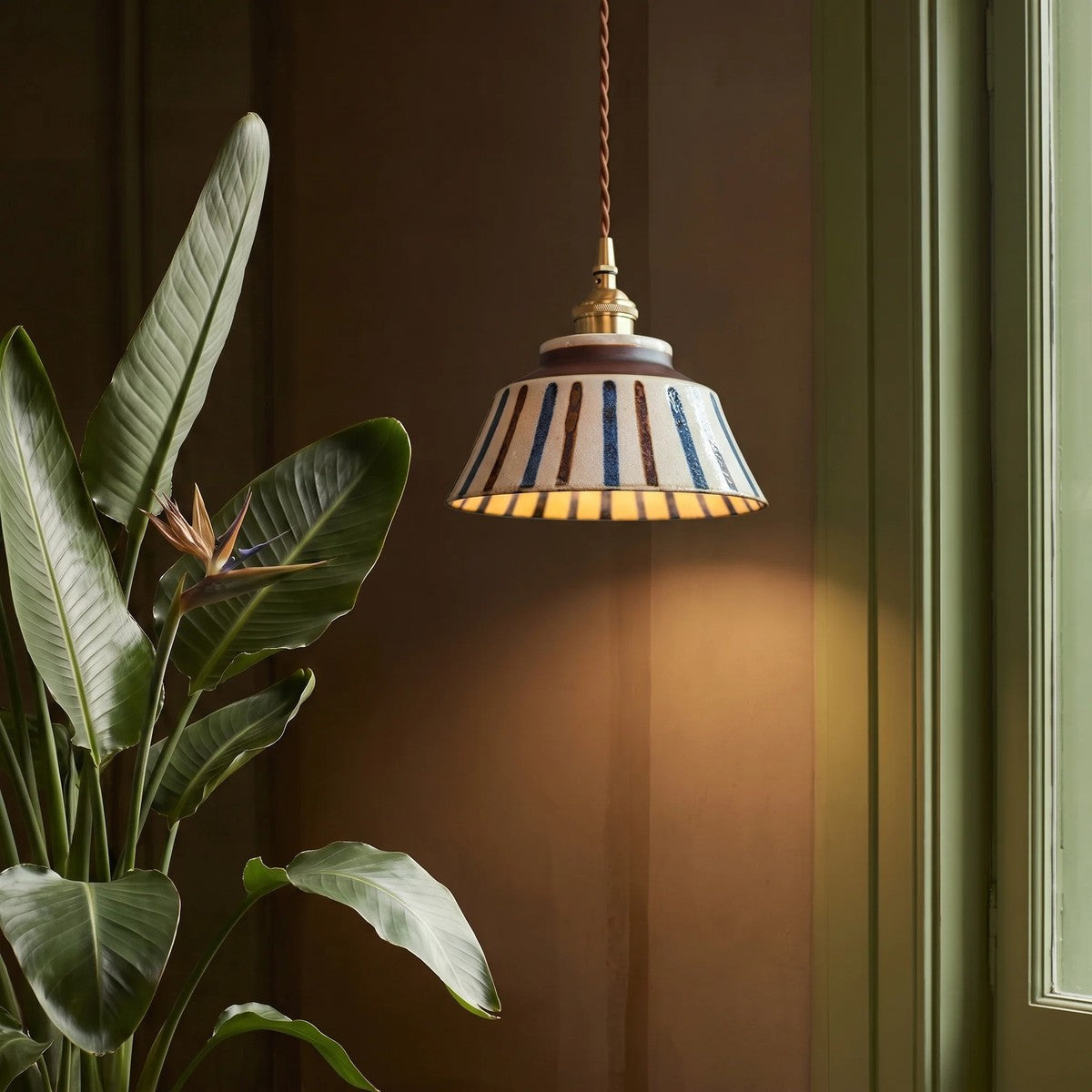 Hana striped ceramic pendant light lit against a green wall