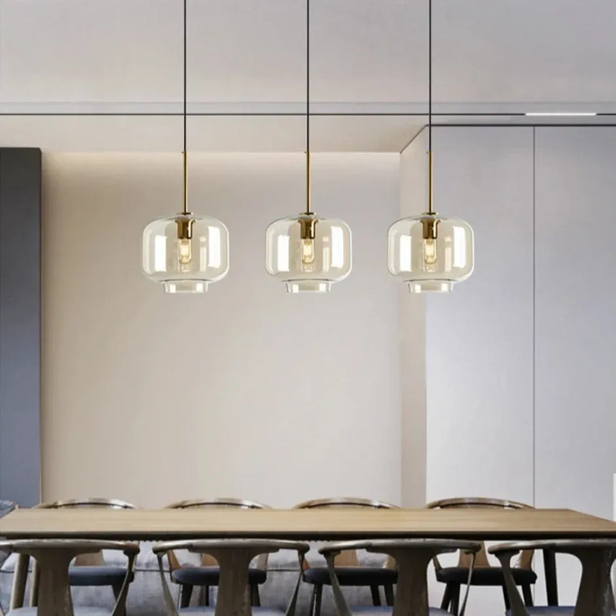Three Ambra amber glass jar pendant lights in a row above a wood dining table