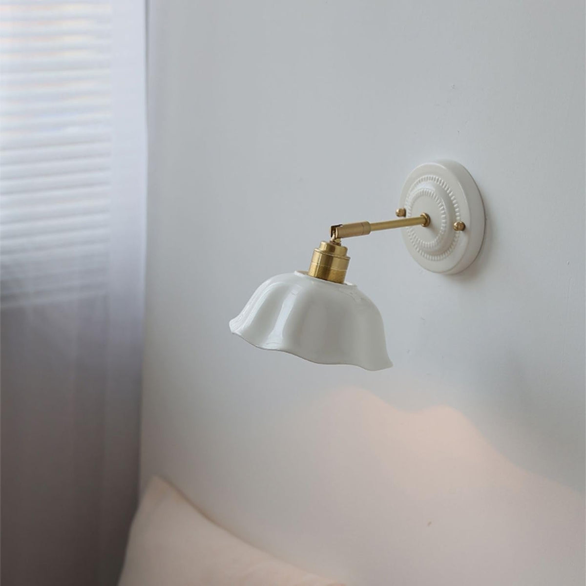 Celia white scalloped ceramic wall sconce above a bed, lighting the wall