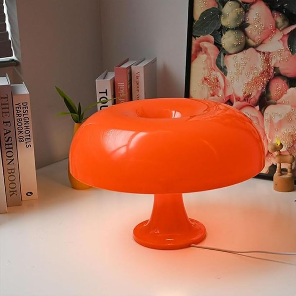 Cepe orange 70s mushroom table lamp glowing on a desk by a bookshelf