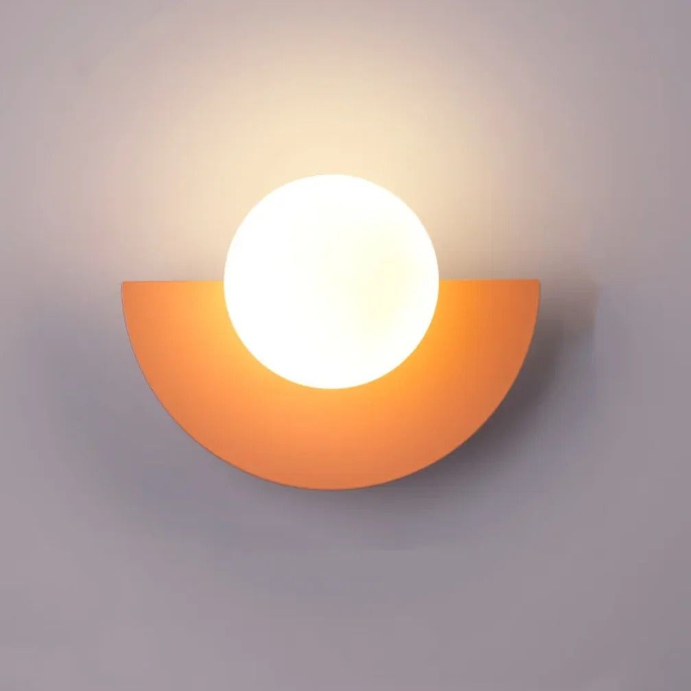 Cleo semicircle globe wall sconce in peach, white glass globe with warm glow on a wall