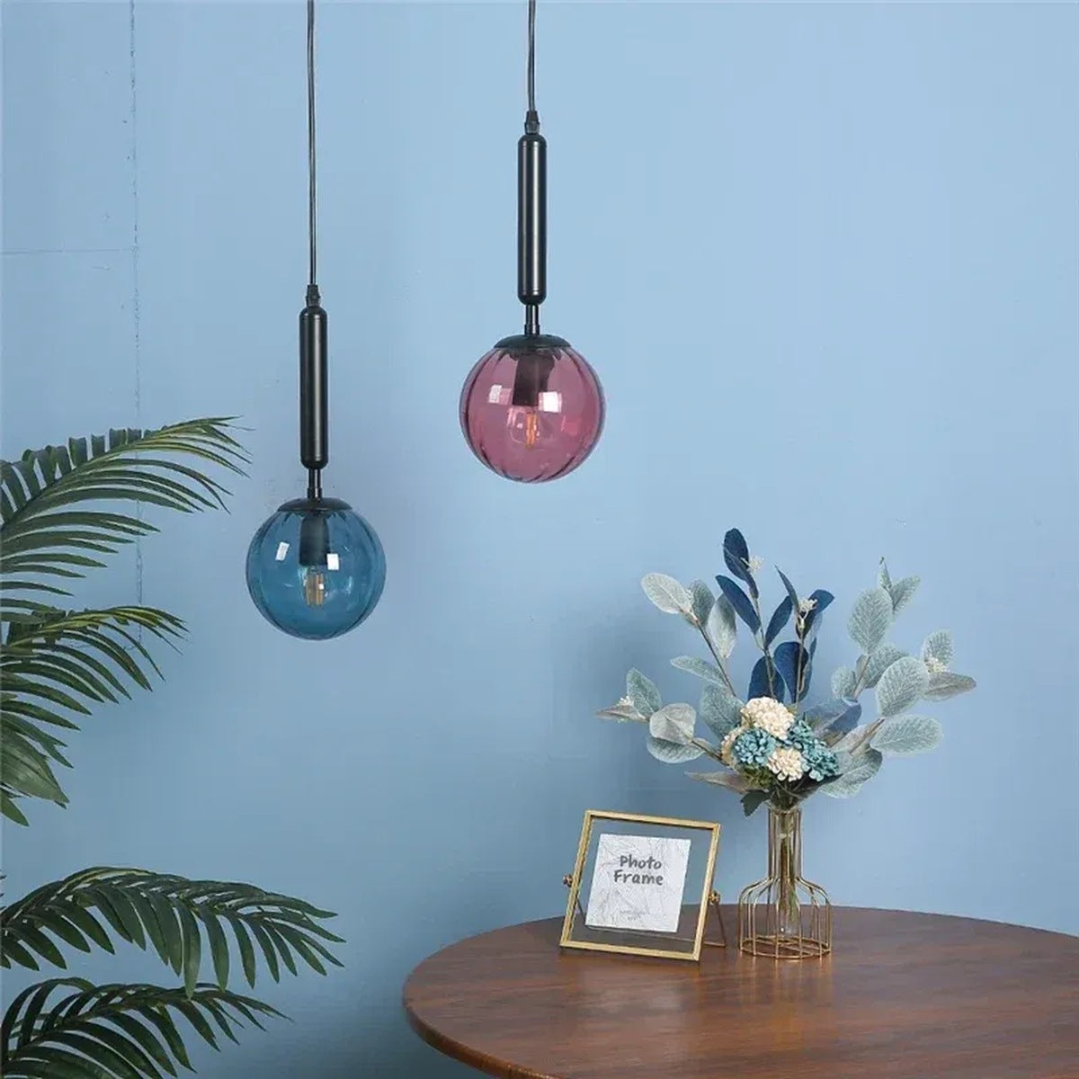 Coco glass globe pendant lights with black stems in blue and pink glass above a dining table