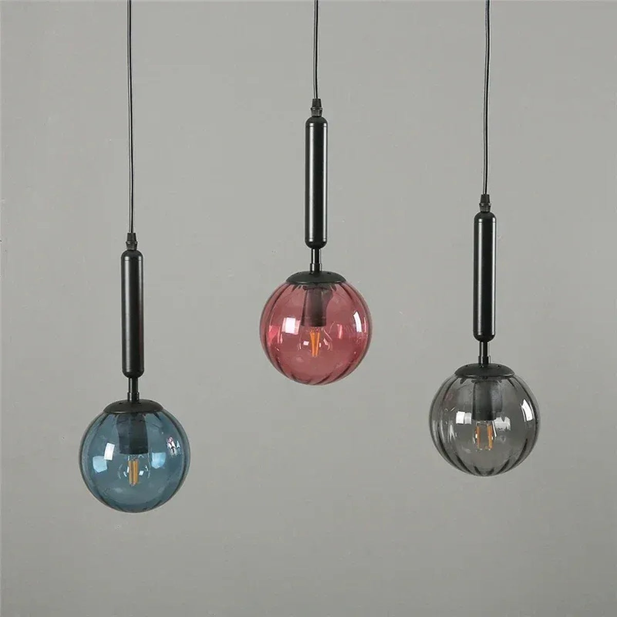 Three Coco glass globe pendant lights with black stems in blue, pink and smoke gray glass