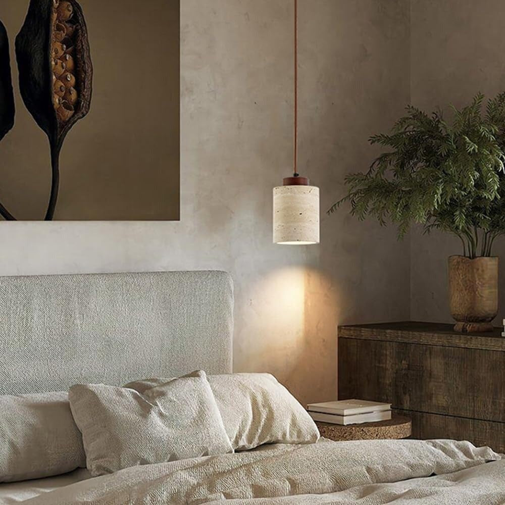Cora travertine cylinder pendant light glowing beside a bed against a plaster wall