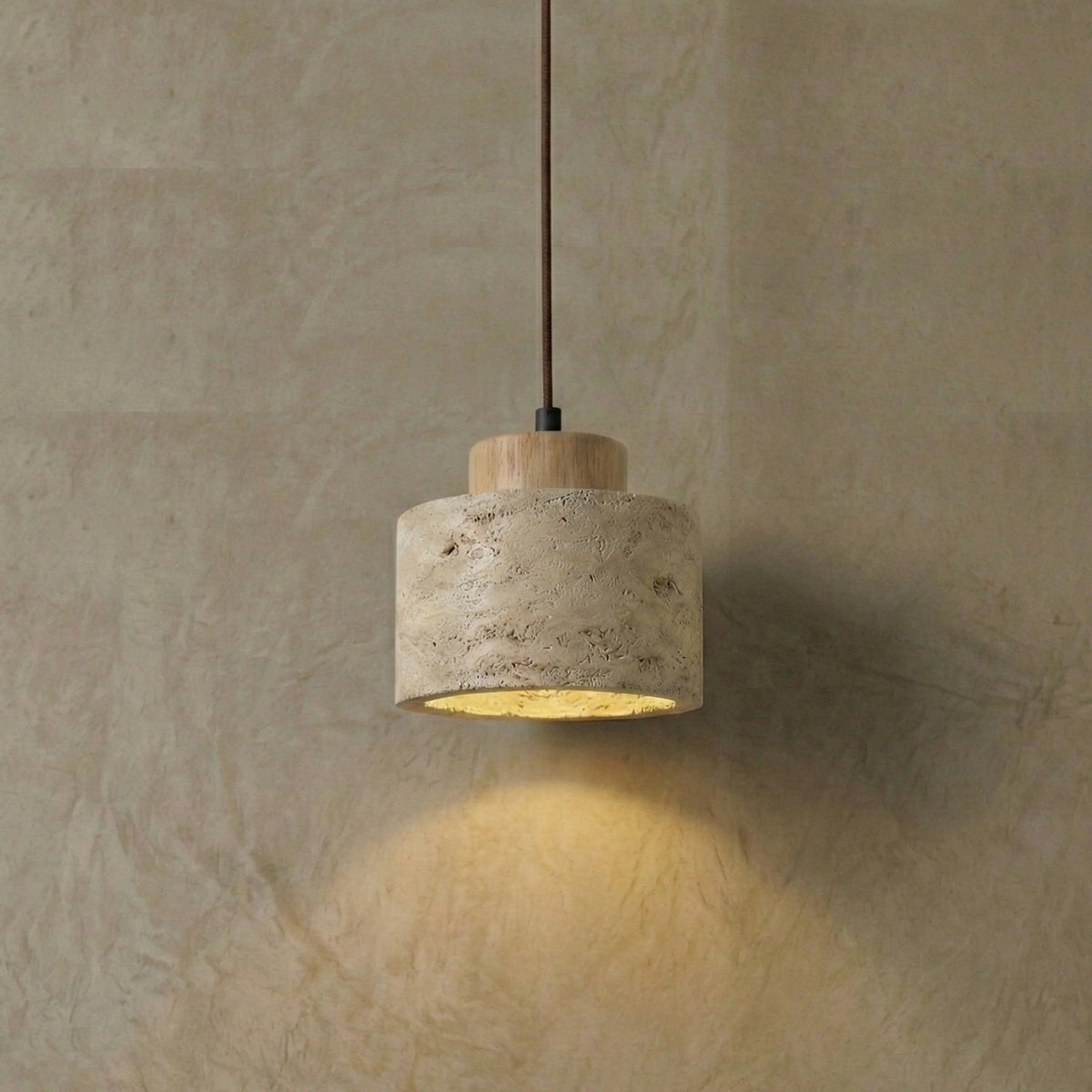 Cora travertine drum pendant light switched on against a plaster wall