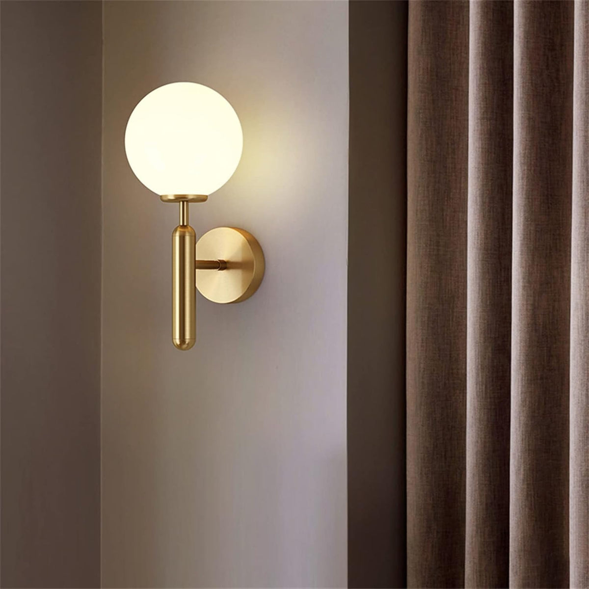 Elio gold globe wall sconce lit beside a curtain