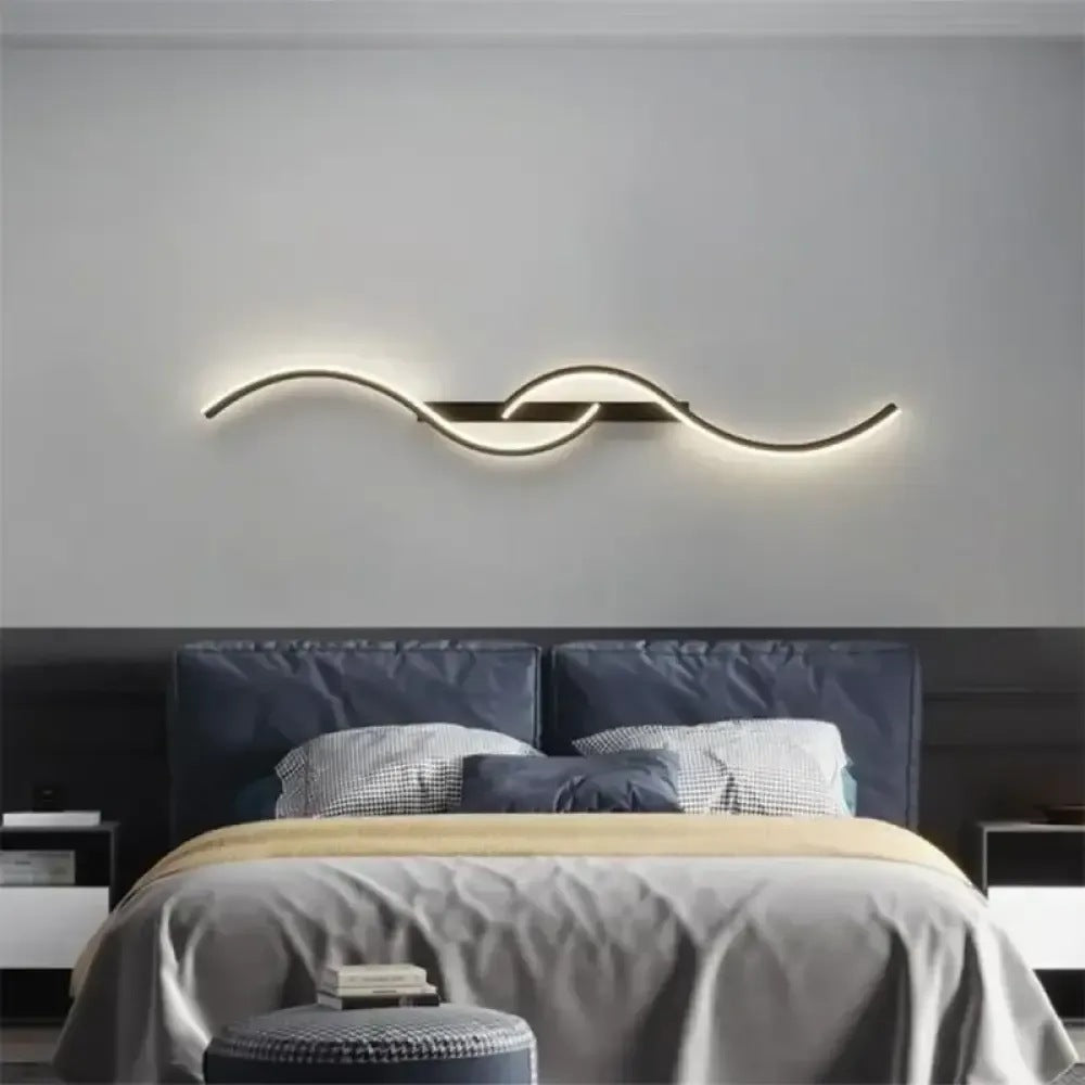 Lyra black wave LED wall sconce mounted horizontally above a bed