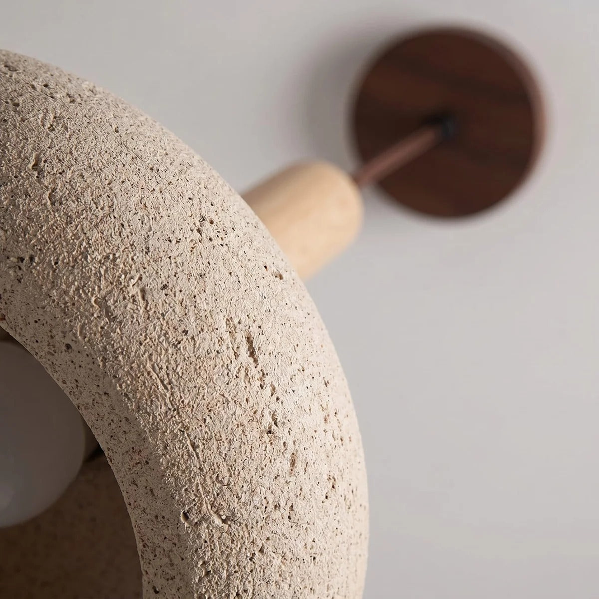 Close-up of the natural travertine texture, light wood stem and walnut-tone canopy of the Mila pendant