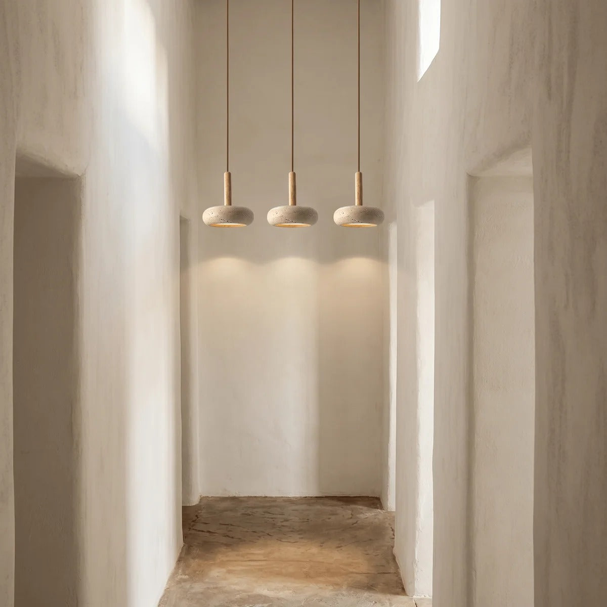 Three Mila travertine pebble pendant lights hanging in a row in a white hallway