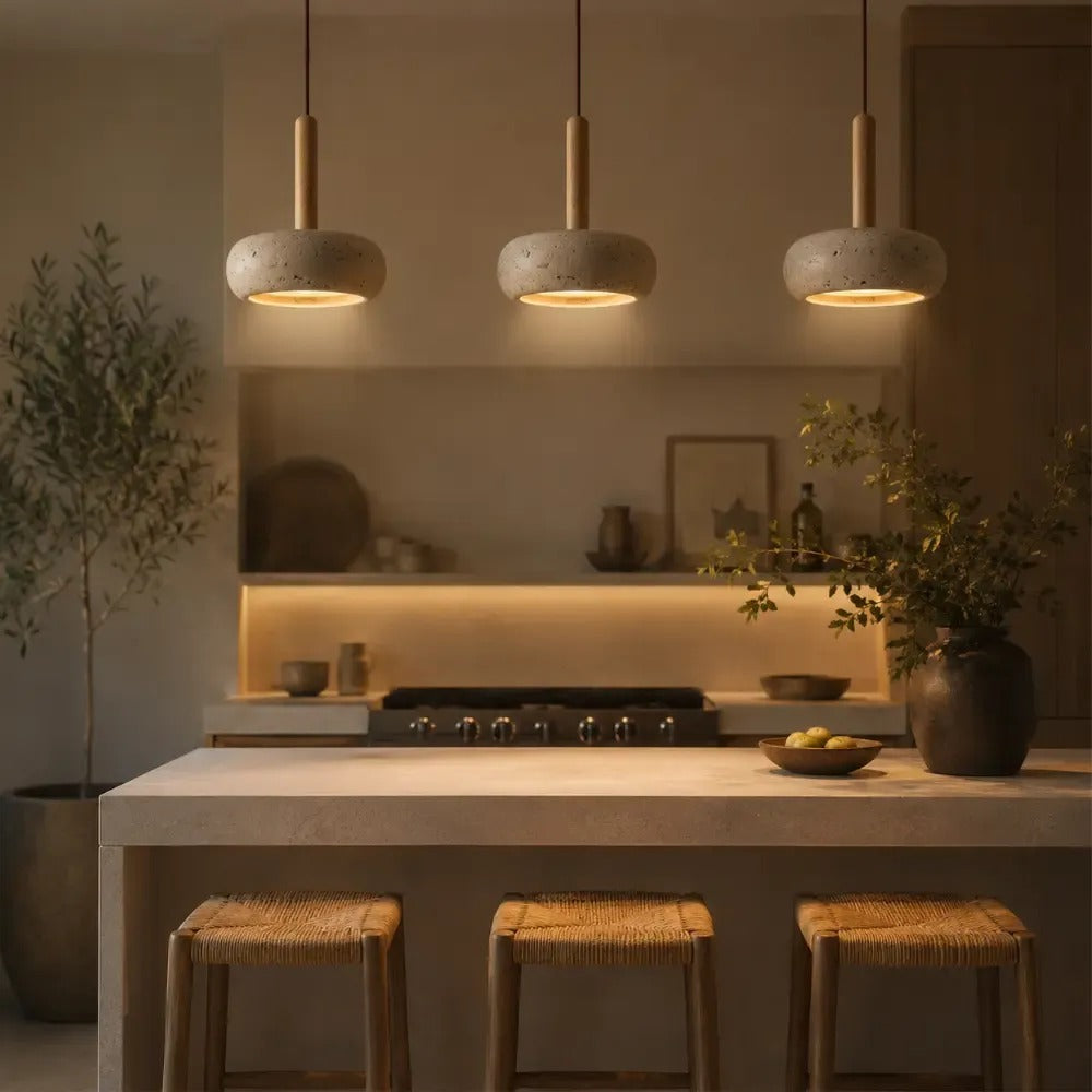 Three Mila travertine pebble pendant lights above a stone kitchen island with woven stools