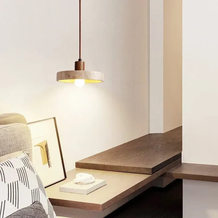 Runa travertine disc pendant light with walnut wood stem beside a bed
