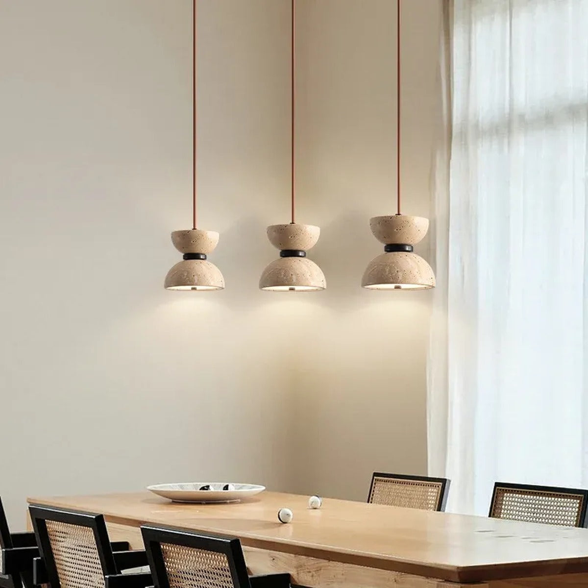Three Sable travertine hourglass pendant lights in a row above a wood dining table