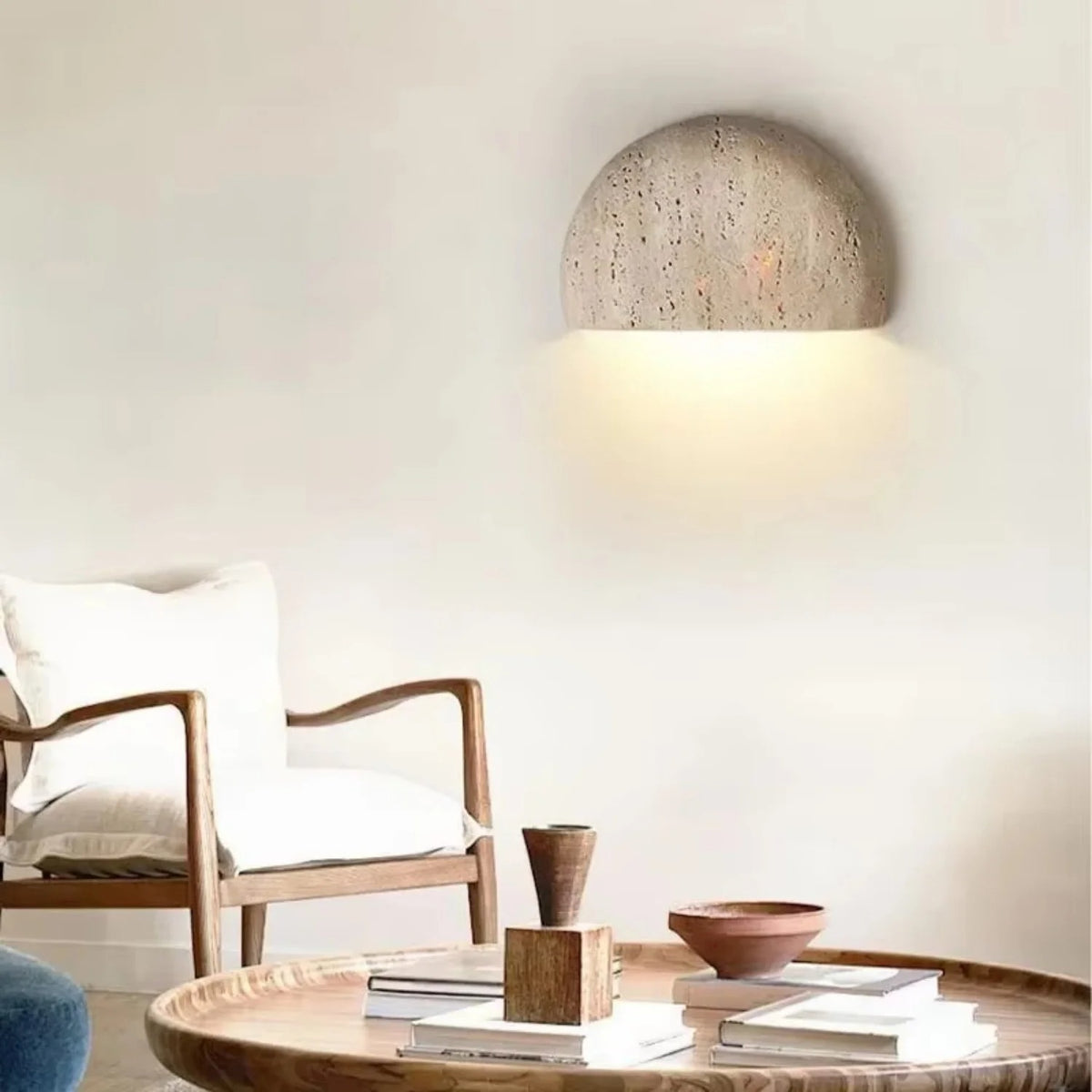 Sora half-moon travertine wall sconce above a reading chair in a living room